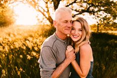 an older man and woman embracing each other in front of some tall grass at sunset