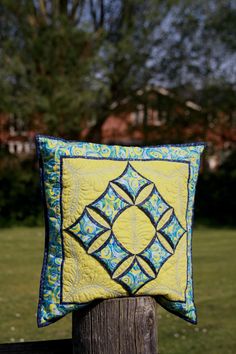 a yellow and blue quilted pillow sitting on top of a wooden post in the grass