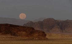 the moon is setting in the sky over some mountains and desert land with no people on it