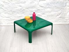 a green table with yellow plates on it and a pink vase sitting on top of it