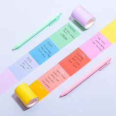 three rolls of colored sticky notes next to a pen and pencil on a white surface