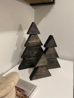 a wooden christmas tree sitting on top of a white table next to a book and bowl