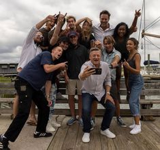 a group of people standing on top of a wooden pier posing for a photo with their cell phones