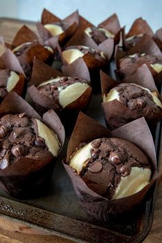 chocolate cupcakes with white frosting and chocolate chips in wrappers on a baking sheet