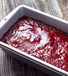 a square casserole dish filled with sauce on top of a wooden table next to a fork