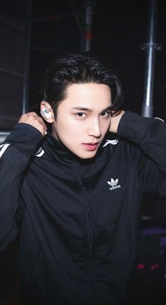 a young man in a black adidas jacket holding his earphones to his ears