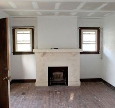 an empty room with a fireplace and two windows