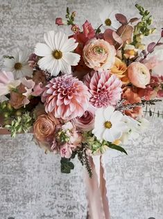 a bouquet of flowers is sitting on a table next to a gray wall with white and pink flowers