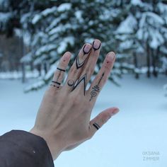 a person's hand with tattoos on it in front of snow - covered trees