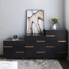 a black dresser with gold handles and drawers in a room next to a painting on the wall