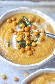 two white bowls filled with soup and garnished with chickpeas on top