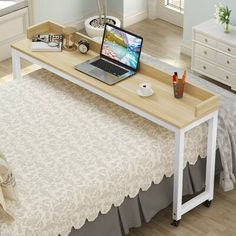 a laptop computer sitting on top of a white desk next to a bed in a room