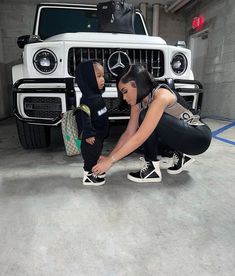 a woman kneeling down next to a child in front of a mercedes benz car with the hood up