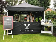 two people standing behind a black tent with all fired up on it