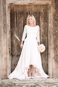 a woman standing in front of a wooden door wearing a white dress and holding a knife