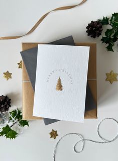 two christmas cards sitting on top of each other next to evergreen leaves and pine cones