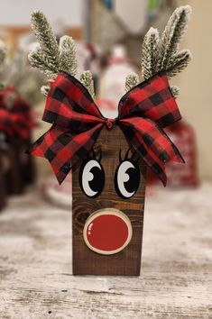 a wooden block with a reindeer head and red nose on it's face, decorated with pine branches