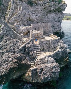 a person standing on top of a cliff next to the ocean with stairs leading up to it