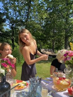 two girls are eating food at an outdoor table with flowers in vases on it