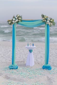 an outdoor ceremony setup on the beach with flowers and blue draping over it