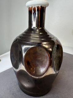 a large metal vase sitting on top of a table next to a white and black wall