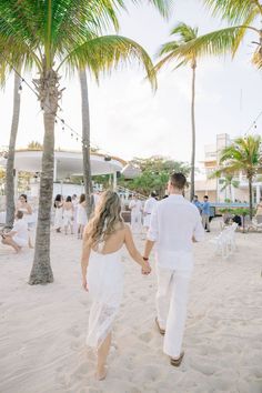 a man and woman walking on the beach holding hands with palm trees in the background