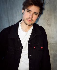 a young man in a black jacket and white t - shirt posing for a photo