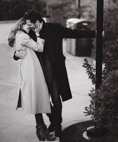 black and white photograph of a man and woman kissing on the street while holding each other's hands