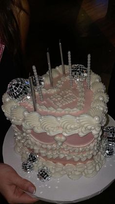 a white cake with pink frosting and disco balls on top is being held by a woman