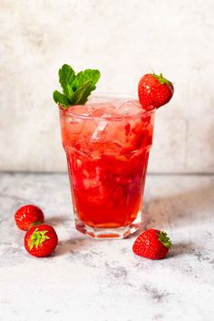 a glass filled with ice and strawberries on top of a white table next to two strawberries