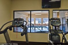 there are two treadmills in the gym with an indoor swimming pool behind them