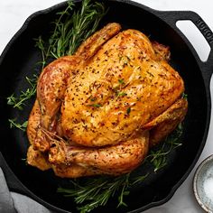 a chicken in a skillet with herbs on the side