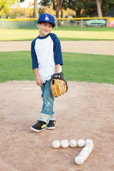 a young boy holding a catchers mitt next to some balls on the field