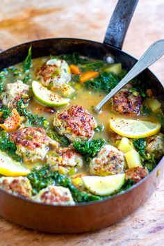 a pan filled with meatballs and vegetables on top of a wooden table next to a spoon