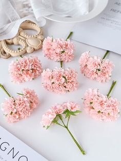 pink carnations are arranged on a table next to a white plate and other items