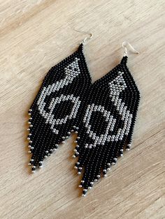 a pair of black and white beaded earrings sitting on top of a wooden table