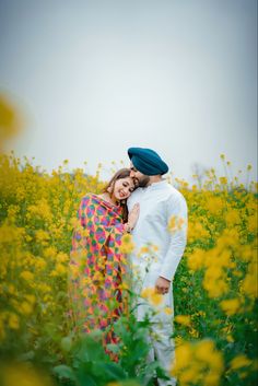 a man and woman standing next to each other in the middle of a field full of yellow flowers