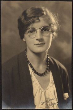 an old black and white photo of a woman wearing glasses with a necklace on her neck