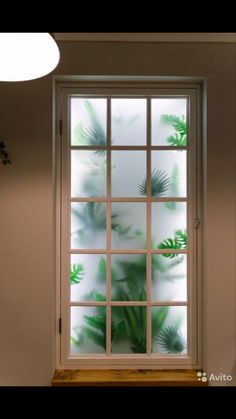 an open window with green leaves on it in front of a white wall and light fixture