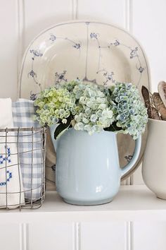 a blue pitcher filled with flowers sitting on top of a counter next to plates and utensils