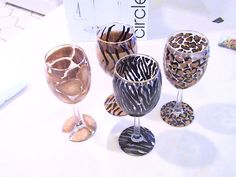 four wine glasses with animal print designs on them sitting on a white tableclothed surface