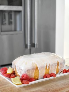 a white frosted cake with raspberries and lemons on a plate in front of an oven