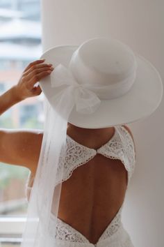 the back of a woman wearing a wedding dress and white hat with a veil on her head