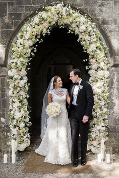 a bride and groom standing in front of an arch with flowers on it at their wedding