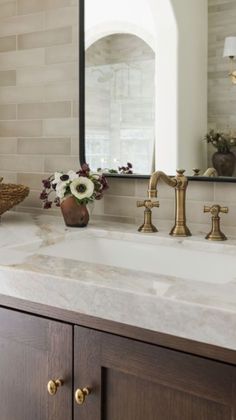 a bathroom sink with two faucets and a mirror above it that has flowers on the counter