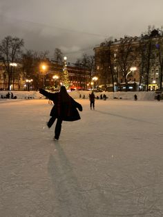 a person skating on an ice rink in the middle of town at night with people walking around