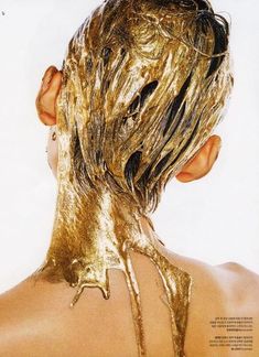 the back of a woman's head is covered in gold paint and has her hair pulled back