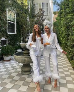 two women dressed in white posing for the camera with plates of food on their feet