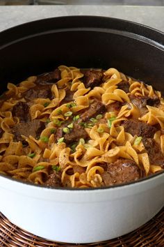 a pot filled with pasta and meat on top of a wicker place mat next to a wooden table