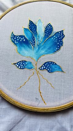 a close up of a blue flower on a white cloth with gold trimmings